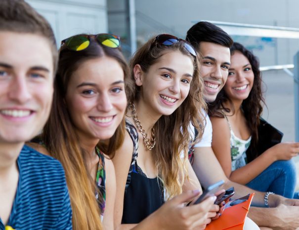 Portrait of group of students having fun with smartphones after class.