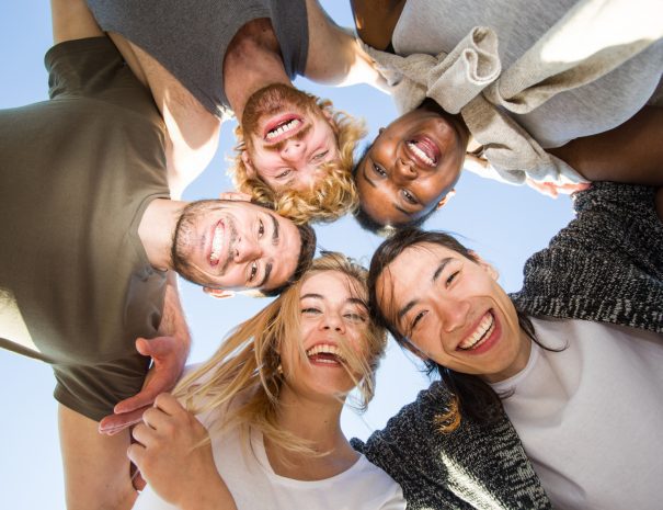 Cheerful friends huddling against blue sky on sunny day